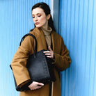 Vesken Tromsø i klassisk sort vist fram av modell i en beige kåpe. En jobbveske for som rommer mye. [wv]