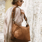 Romslig hverdags-veske i Ku skinn, flettet skulderreim, glidelås-lukning og skinn-frynse detaljer. Veske dame. Skinn Veske til dame. bag. Pc veske dame. Jobbveske dame. Hverdagsveske dame. Skoleveske dame. Reiseveske dame. Stor skinn veske til dame. Barcelona Hippi Grace. Brun veske. Brun skinnveske dame. Lys brun skinnveske dame. Lysebrun veske i ekte skinn.  Crossbodyveske dame. Skulderveske dame. Hippi Grace Barcelona i fargen Nobuck cognac.[wv]